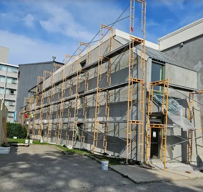 Three-story building covered in scaffolding with a fresh gray EIFS base coat applied across the whole elevation