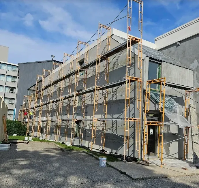 Three-story building covered in scaffolding with a fresh gray EIFS base coat applied across the whole elevation