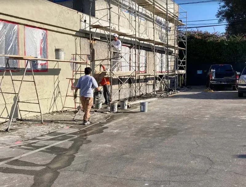 Stucco crew on scaffolding applying a fresh coat to a commercial building with masked windows
