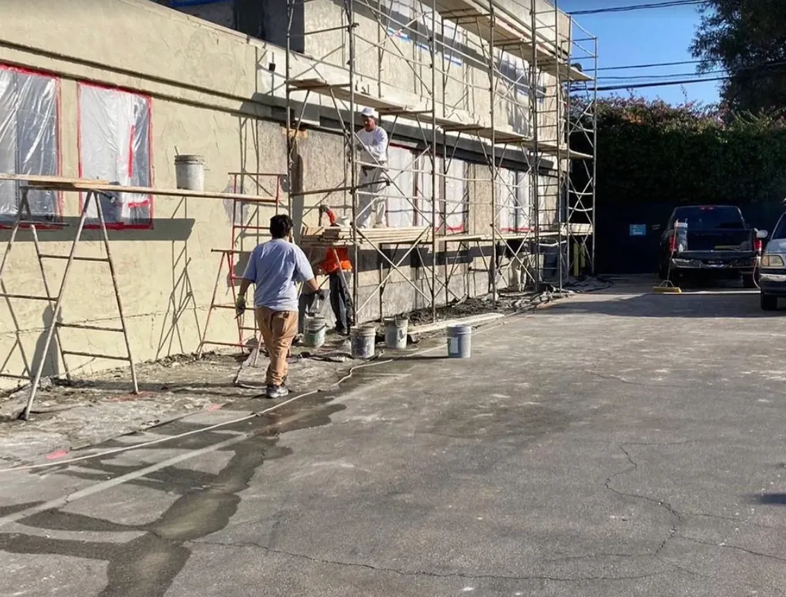 Stucco crew on scaffolding applying a fresh coat to a commercial building with masked windows