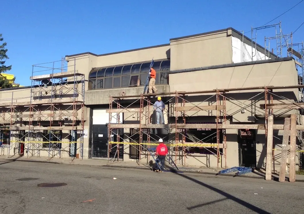 Workers on scaffolding across the front of a two-story tan commercial building during stucco repair