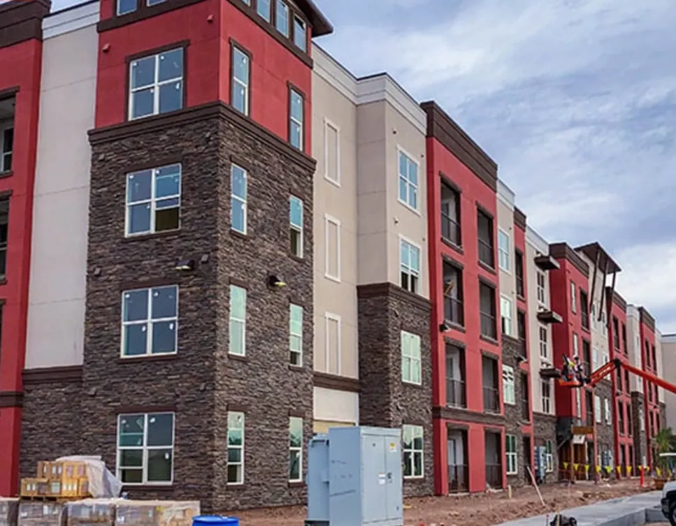 Four-story apartment building with red and tan stucco, dark trim, and stacked-stone corner columns