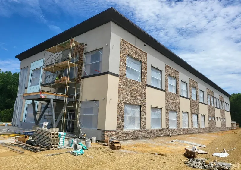 Two-story commercial building with fresh tan stucco between stacked-stone columns, scaffolding still up on one corner