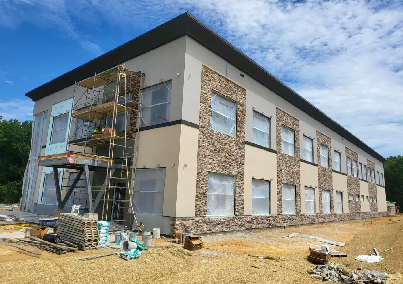 Two-story commercial building with fresh tan stucco between stacked-stone columns, scaffolding still up on one corner