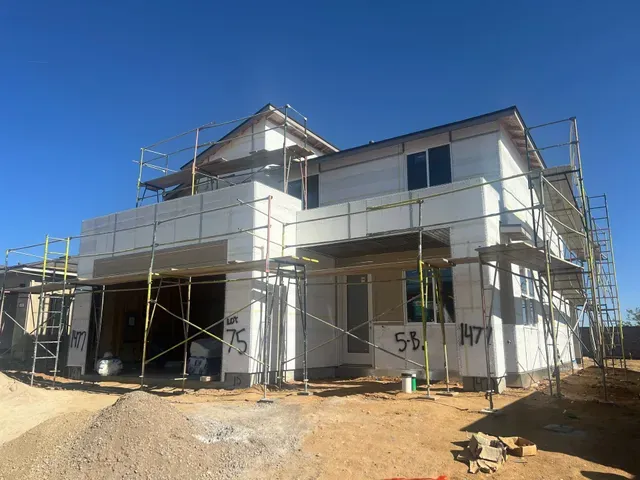 Two-story home under construction wrapped in white foam board and scaffolding, ready for stucco base coat